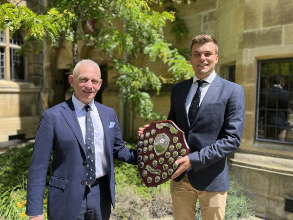 two men stand holding a shield award