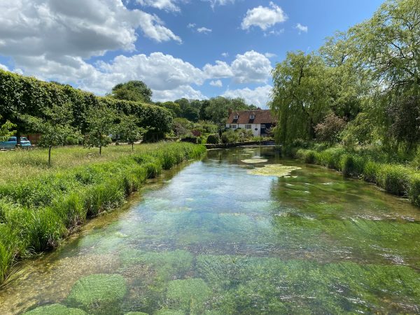 a river with trees and a blue sky leading to a cottage