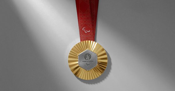 The gold medal from the Paris 2020 Olympics on a red ribbon against a white backround