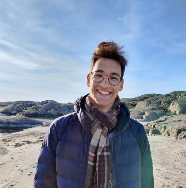 A man in glasses wearing a scarf and a blue warm jacket standing on a mountainous terrain